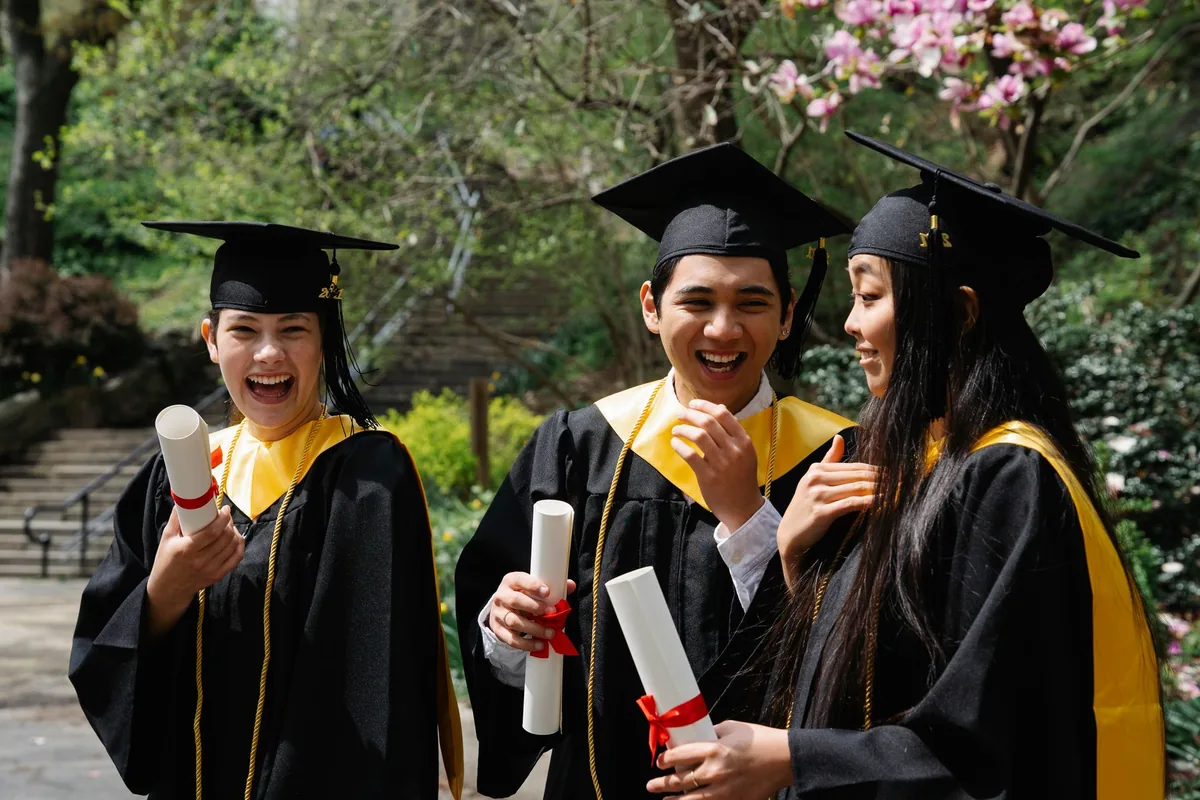 Tres estudiantes con toga y birrete celebran su graduación al aire libre.