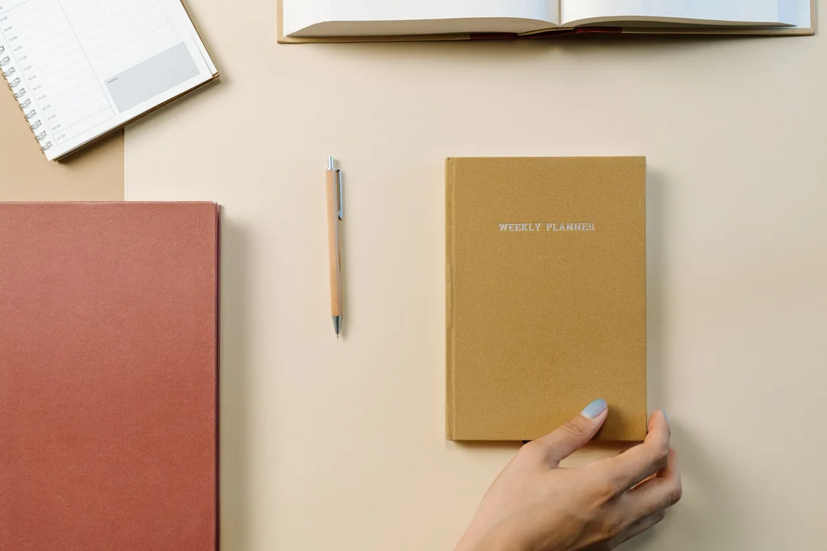 Agenda semanal, cuadernos y bolígrafo sobre un escritorio claro.