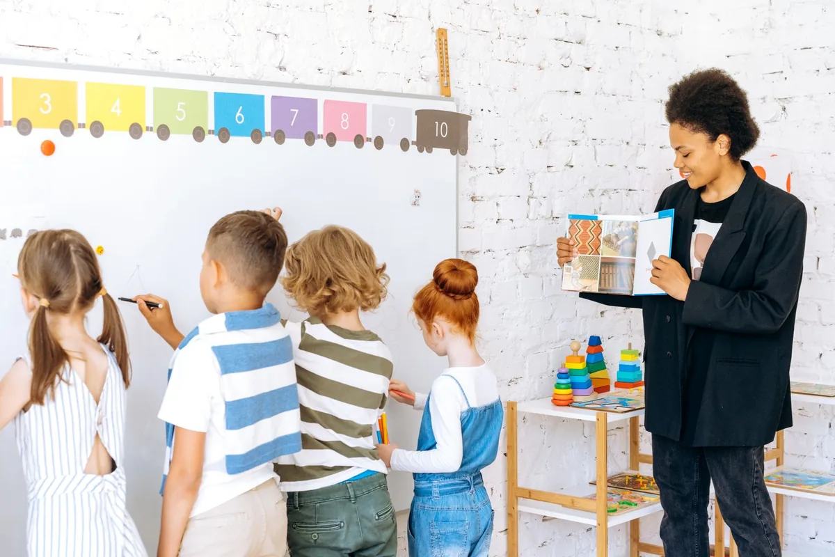 Docente guía una actividad de aprendizaje con niños frente a una pizarra.