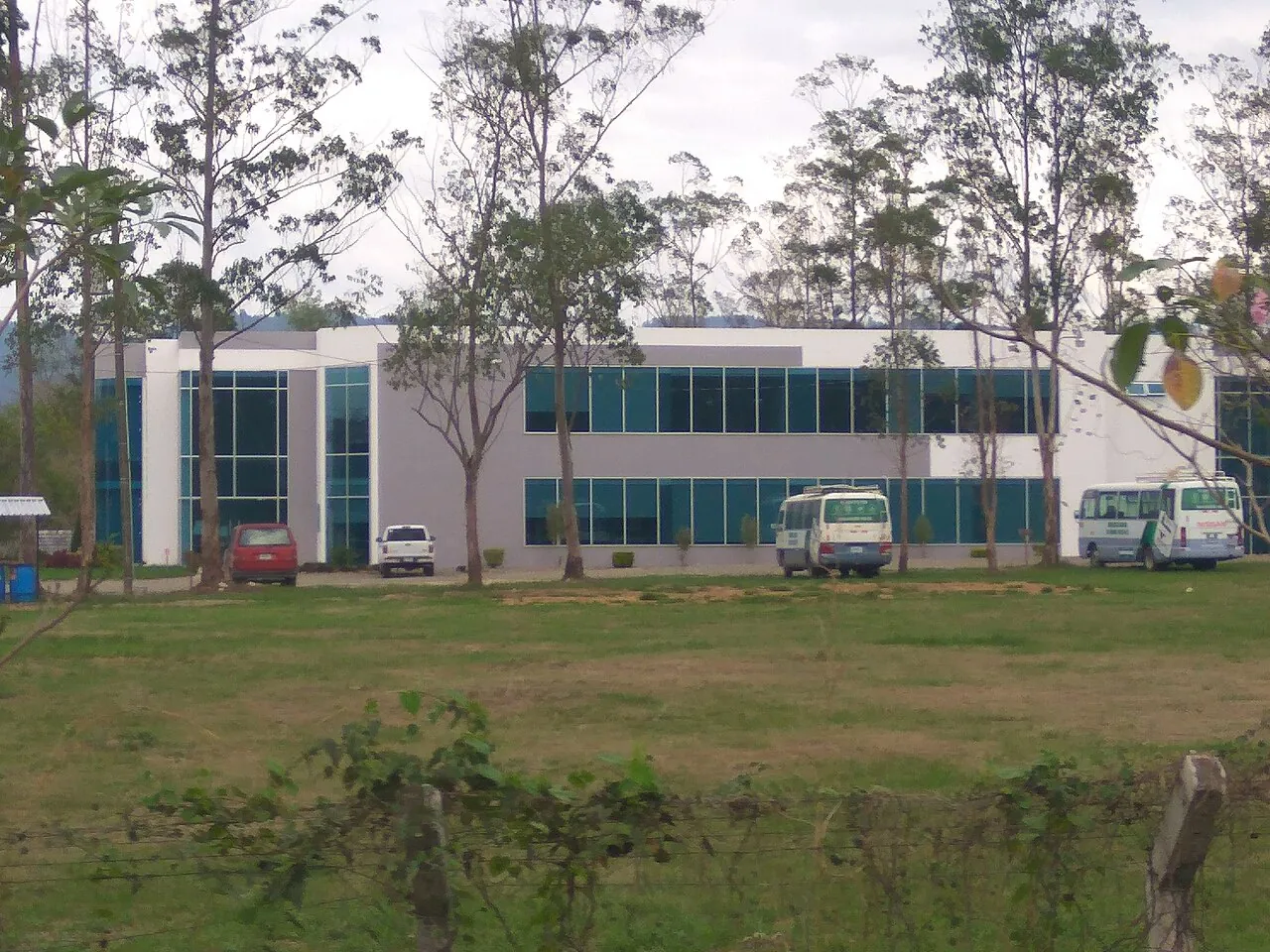 Edificio de UNACIFOR en Siguatepeque, de dos niveles y amplios ventanales, rodeado de árboles y césped.