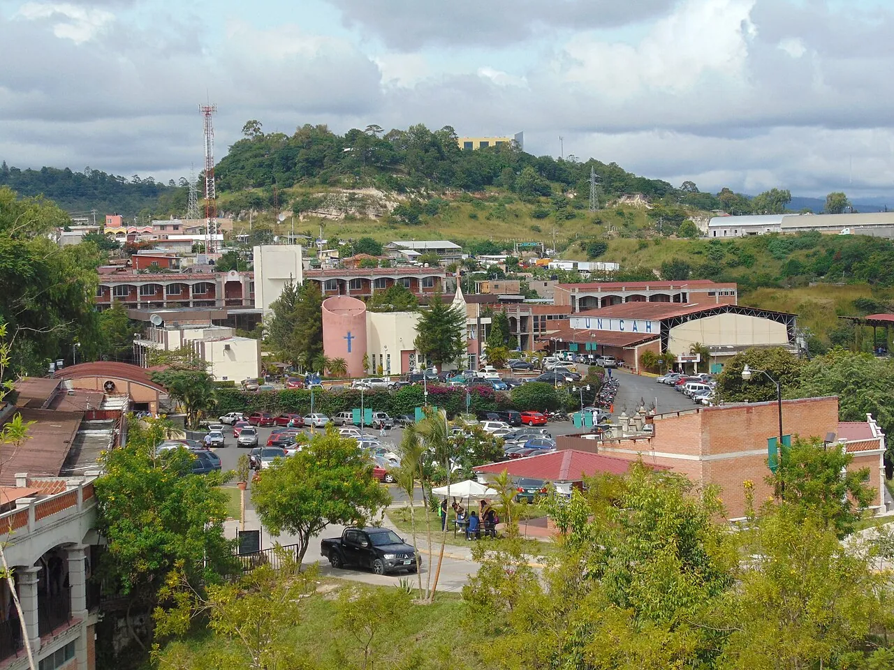Vista del campus Sagrado Corazón de Jesús de UNICAH, con edificios de ladrillo, capilla, estacionamientos y el rótulo UNICAH.