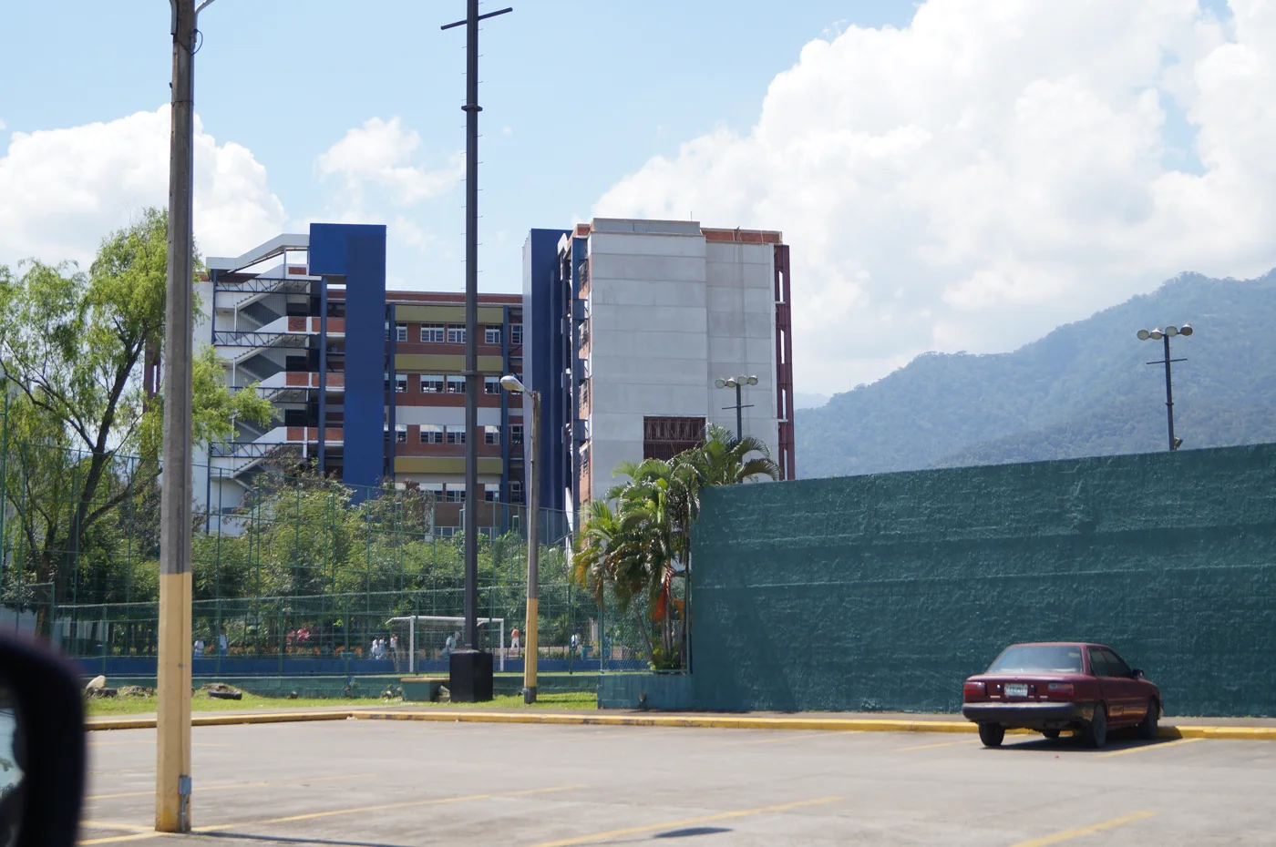 Edificio de la Universidad de San Pedro Sula visto desde la calle, con vegetación y montañas al fondo
